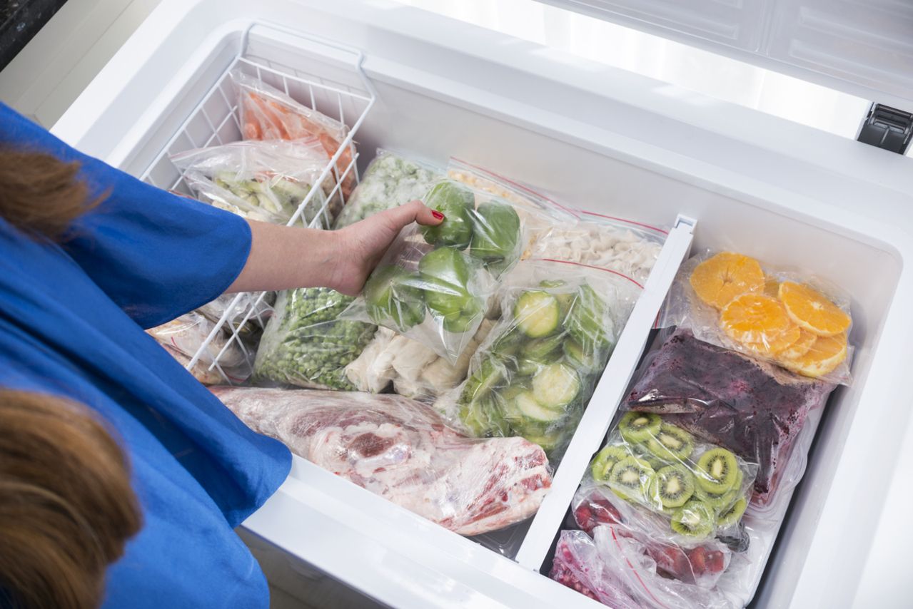 A woman putting green bell peppers into fridge