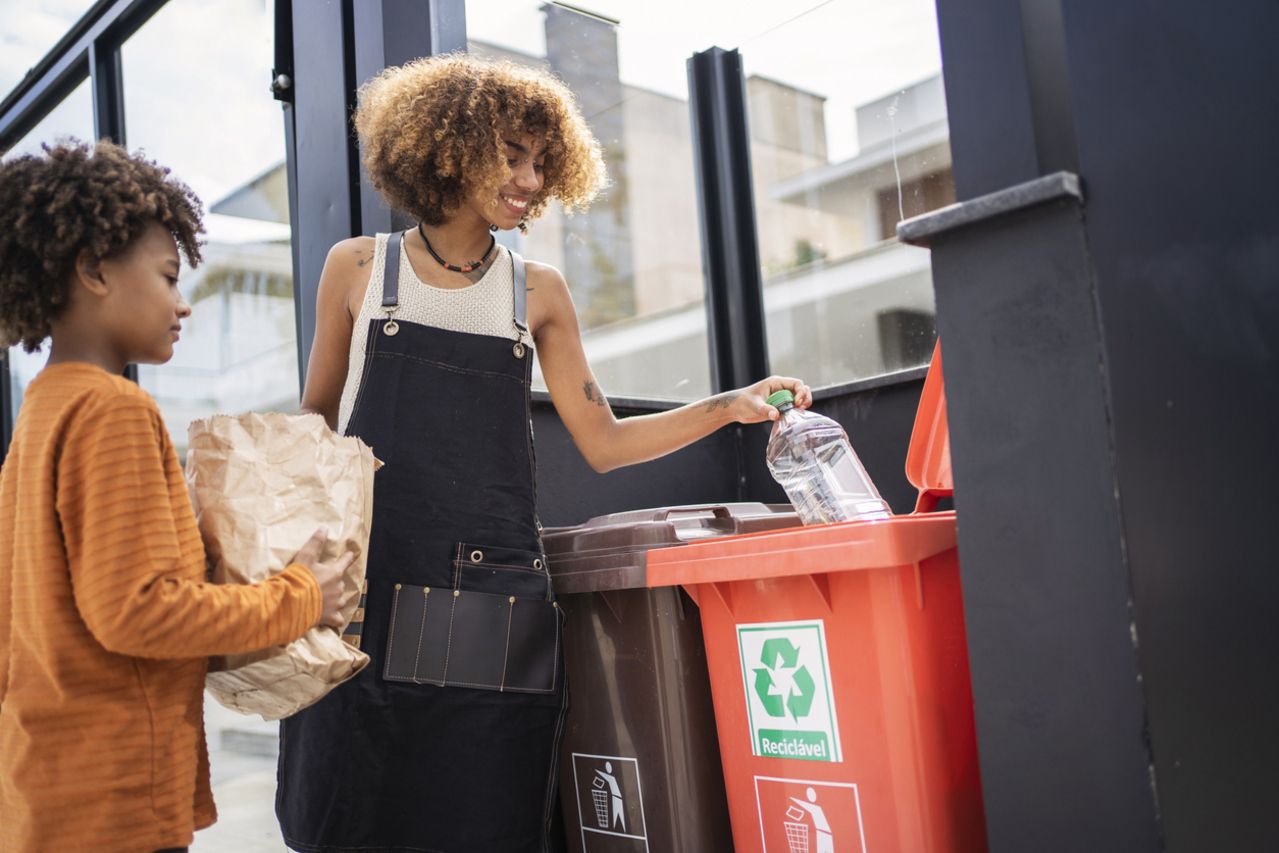 African american young woman and her younger brother recycling garbage. Sustainability concept.