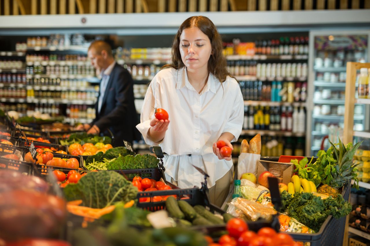 Young girl with a grocery cart  selects fresh vegetables in the supermarket