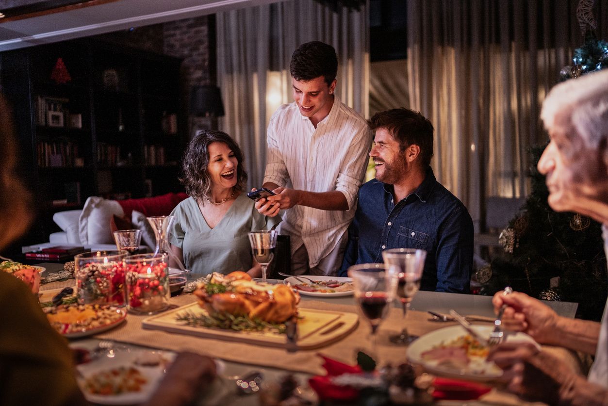 Son showing something on the mobile phone to his parents at Christmas dinner
