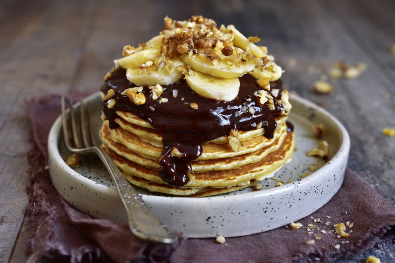 Stack of homemade delicious banana pancakes topped with chocolate sauce, banana slices and walnut